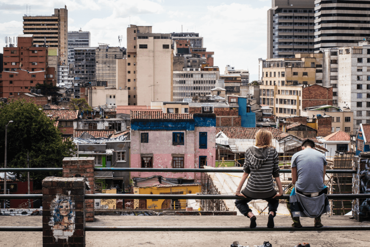 Dos personas jóvenes sentadas en un espacio público, mirando la ciudad. 