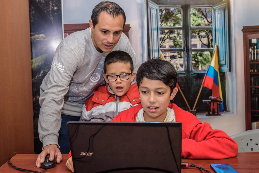 Un hombre mayor le enseña en un computador a dos niños