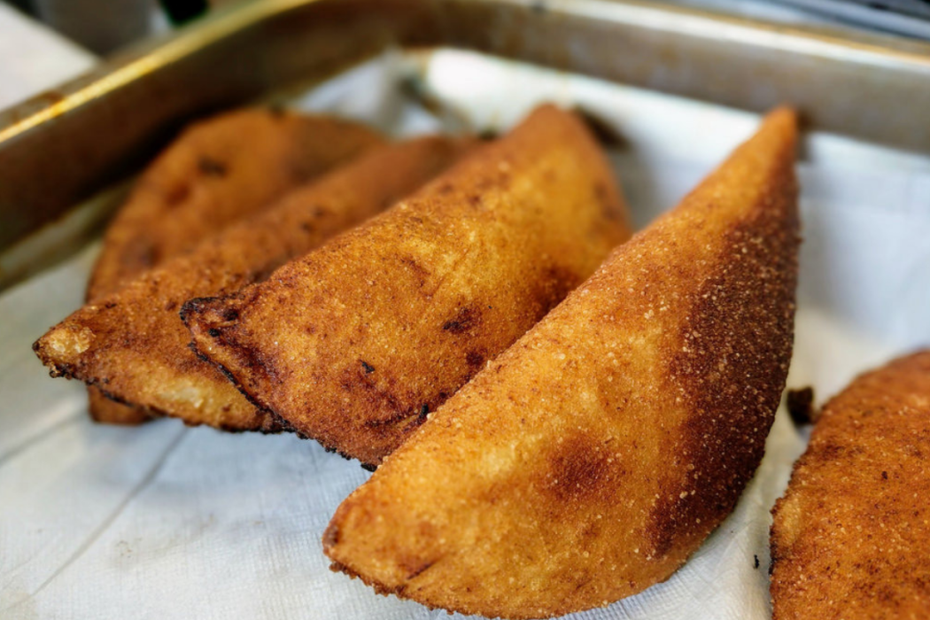 Primer plano de empanadas tostadas escurriendo aceite en una bandeja con papel absorbente.