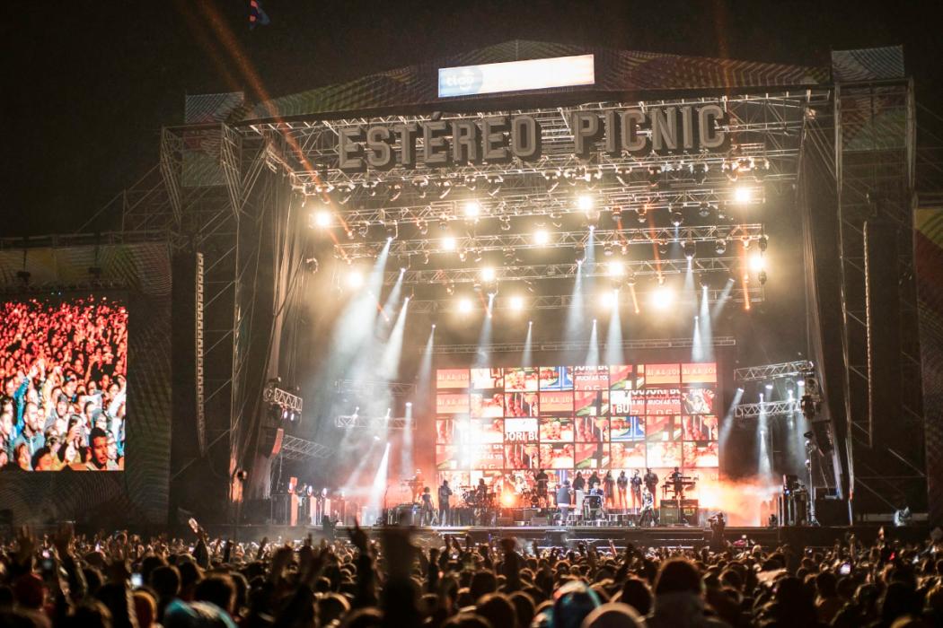 Escenario de noche, iluminado, con público.