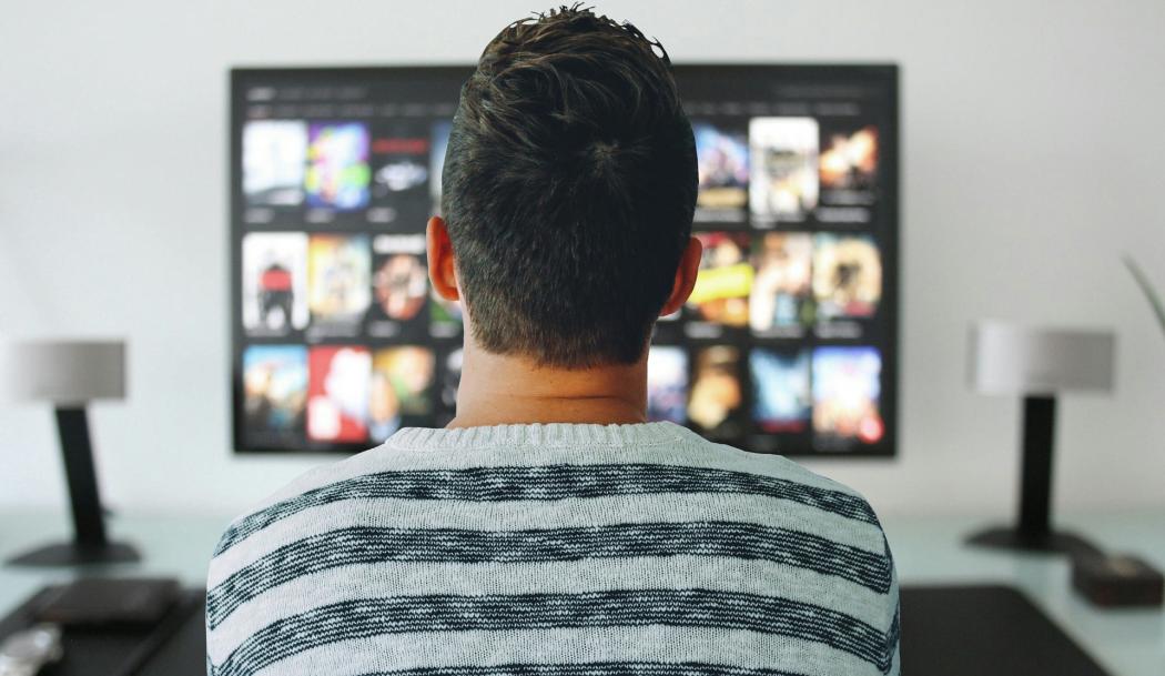 Un hombre de espaldas viendo la pantalla del televisor.