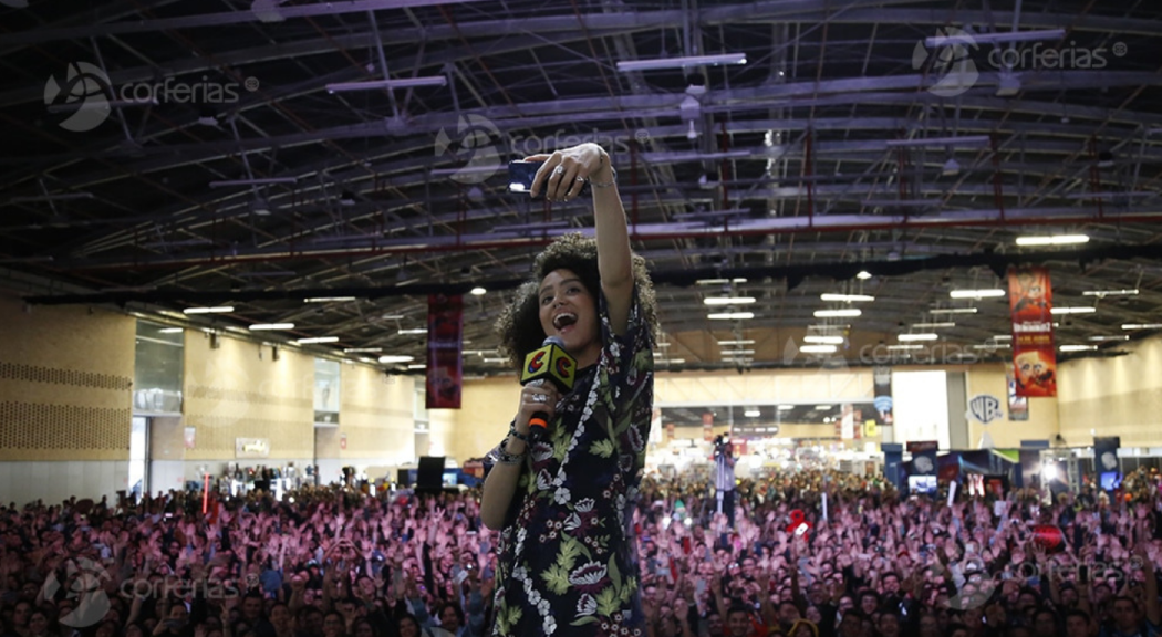 Una mujer morena, con afro, se toma una selfi ante un gran público.