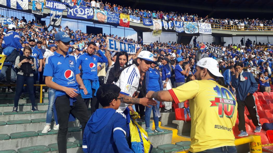 En una gradilla del estadio el Campin, varios hinchas de millonarios conversan entre si 