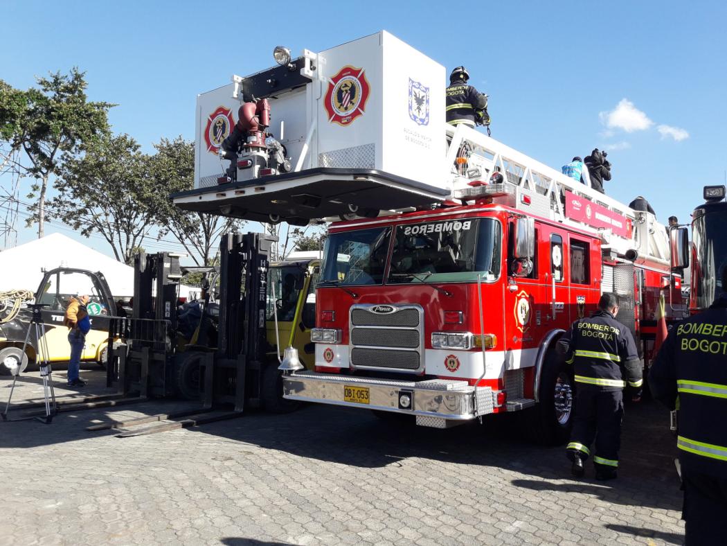 Un carro de bomberos de bogotá estacionado en un parque siendo contemplado por varias personas