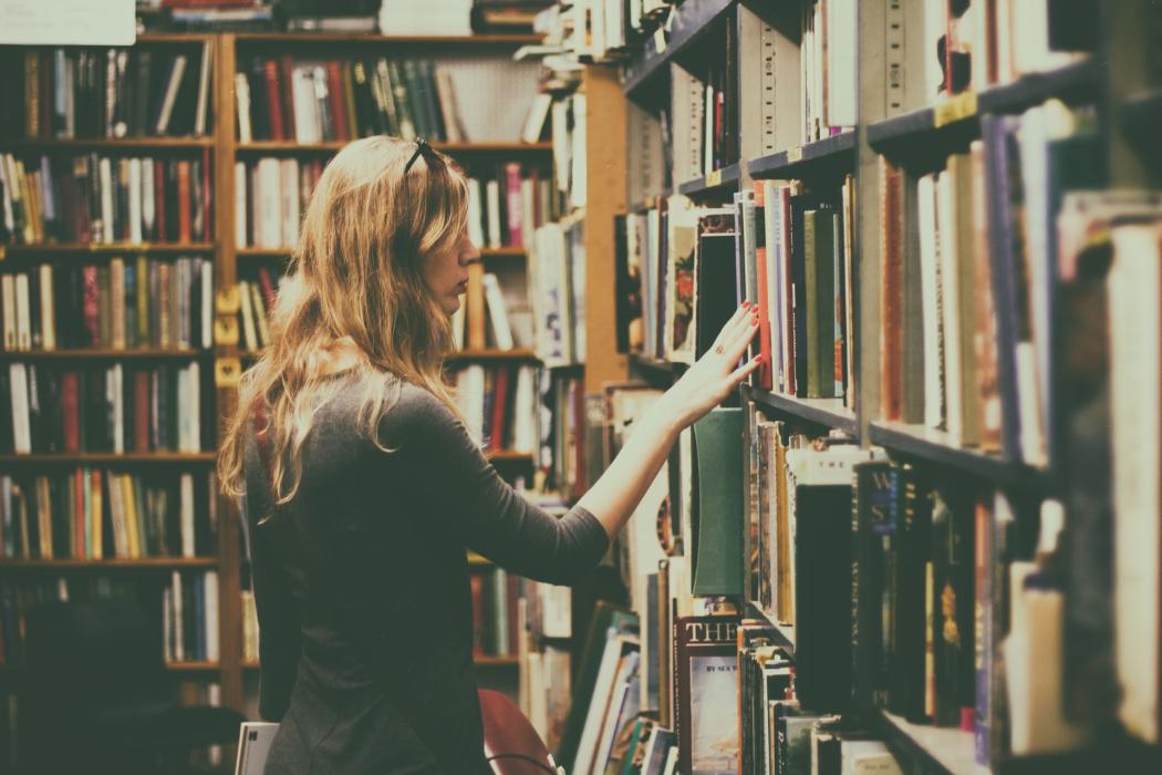 Una mujer recorre con la mano una estantería llena de libros 