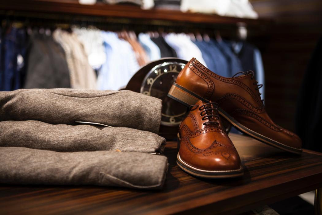 Una foto de unos zapatos cafés de hombre al lado de unas gabardinas 