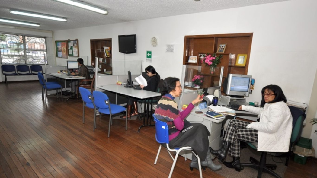 Un salón grande con hartas mesas y cubículos, varias personas hablan entre si en las mesas 