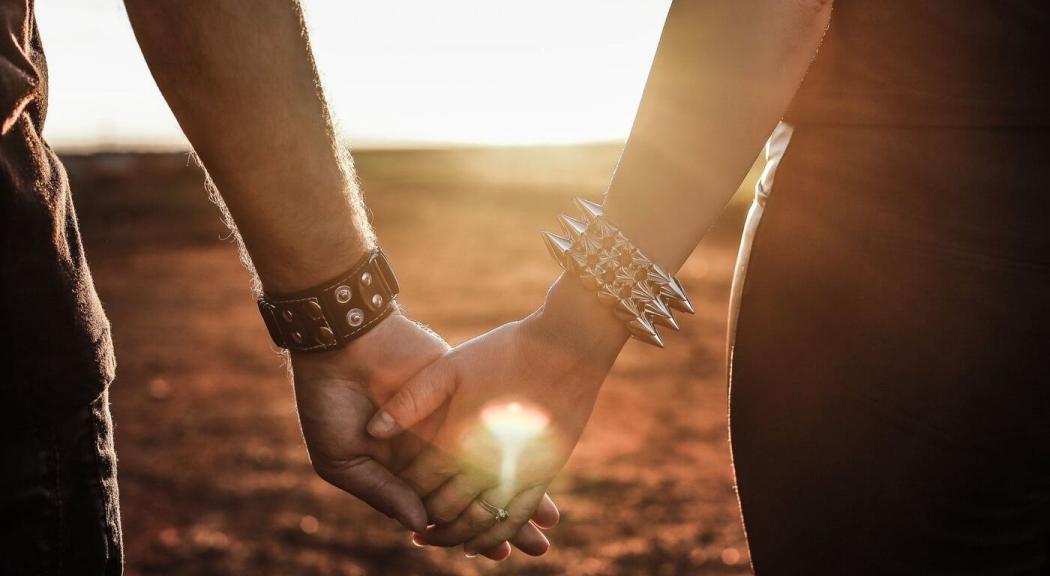 Pareja se agarra de manos, al fondo se aprecia un atardecer.