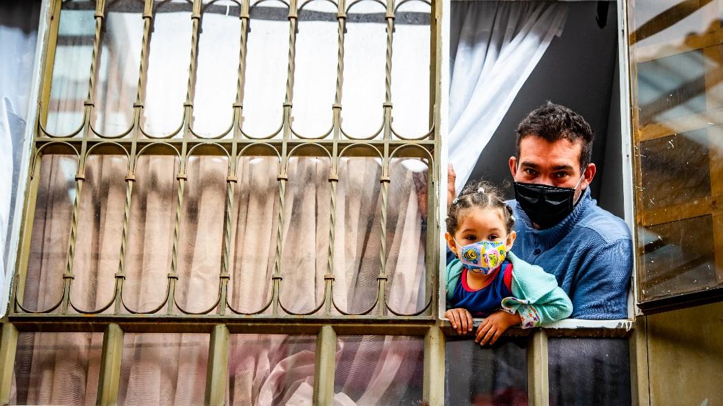 Padre e hija desde una ventana con tapabocas.