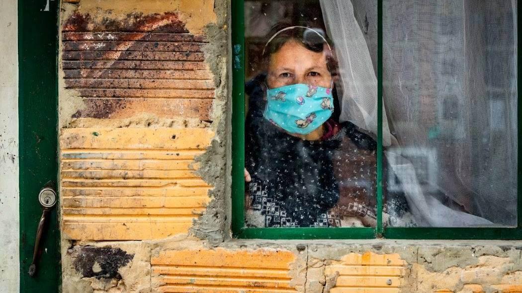 Imagen de una mujer viendo desde su ventana con tapabocas.