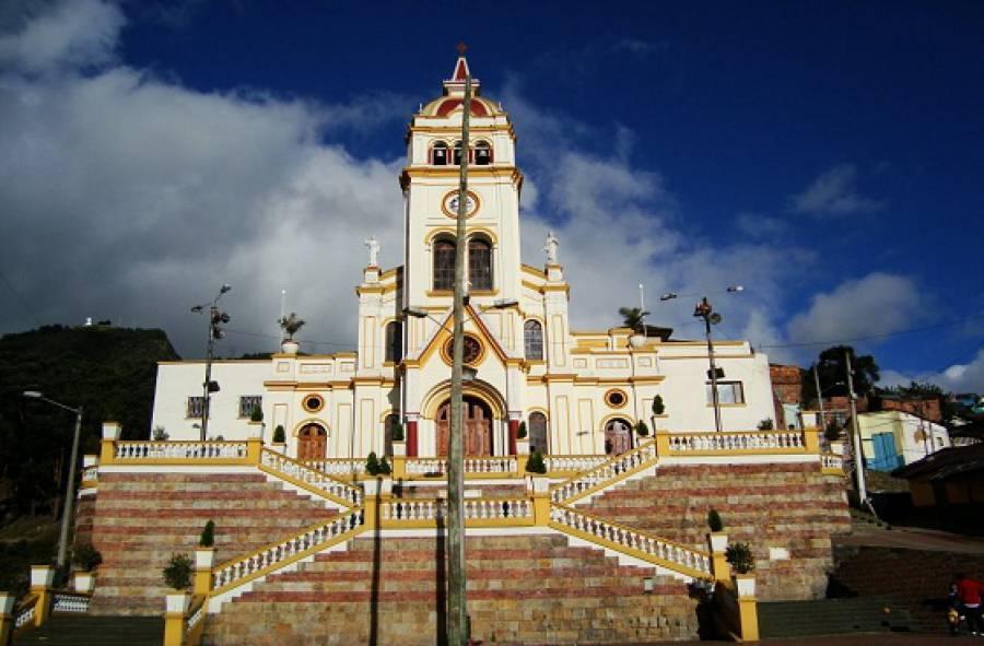 La fachada de una iglesia, de color blanco, con escaleras y un cielo azul en la parte de atras