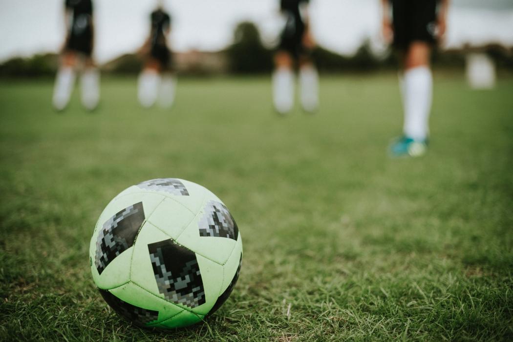 Un balón de futbol en primer plano, atrás se ven jugadores desenfocados