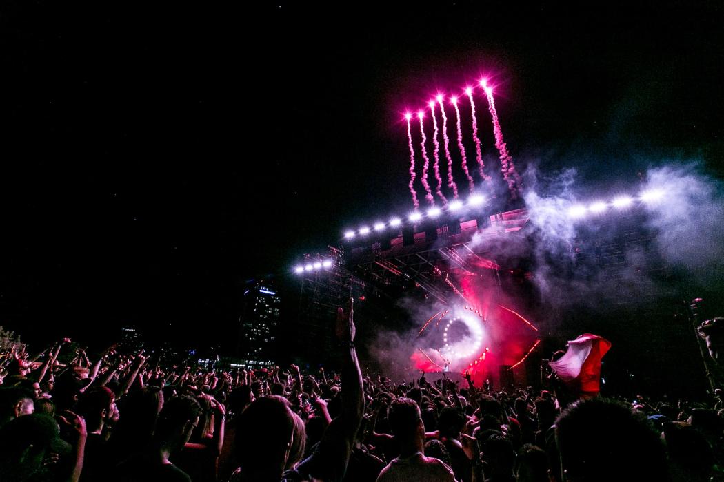 Un concierto donde hay muchas personas alzando las manos, con fuegos artificiales y humo