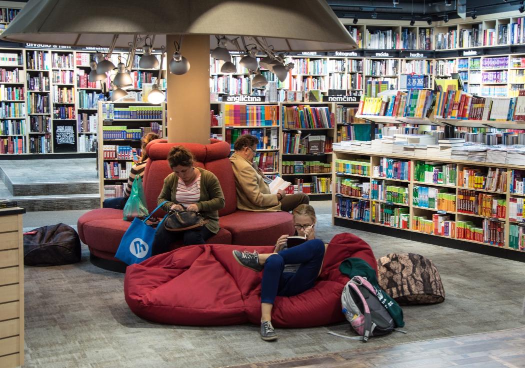 Varias personas sentadas leyendo libros rodeadas de varios estantes de libros 