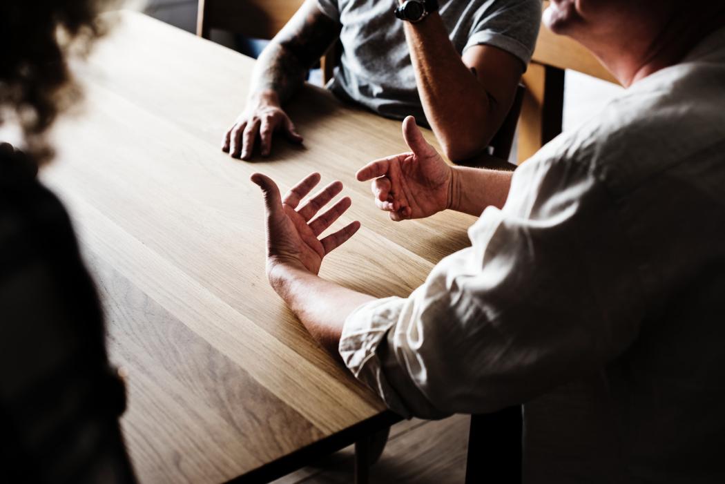 Un grupo de tres personas sentadas en una mesa discutiendo varios temas 