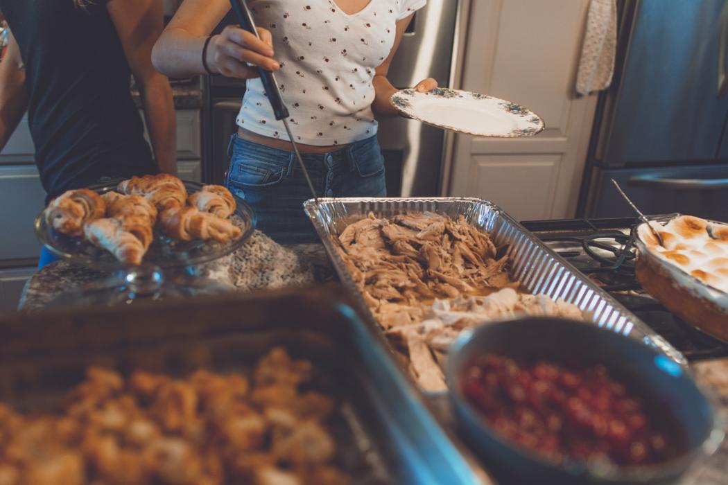 Varias bandejas de comida esparcidas en la mesa con varias personas cogiendo en los platos 