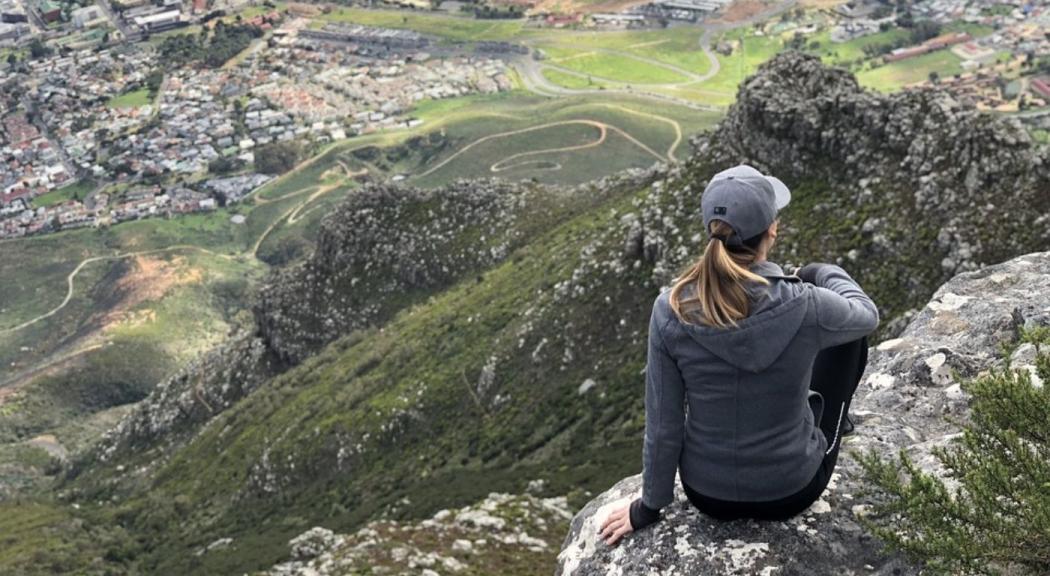 Una mujer de cabello castaño claro se sienta dándole la espalda a la cámara mientras contempla el paisaje.