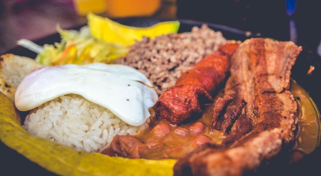 Primer plano de un plato de bandeja paisa con huevo frito, chorizo, chicharrón, arroz, fríjoles, plátano y aguacate.