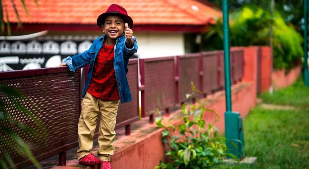 Un niño juega en una baranda, mira a la cámara y extiende su dedo pulgar en señal de aprobación.