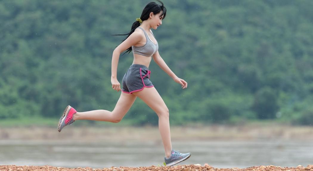 Una mujer blanca de cabello negro trota usando shorts y top corto gris.