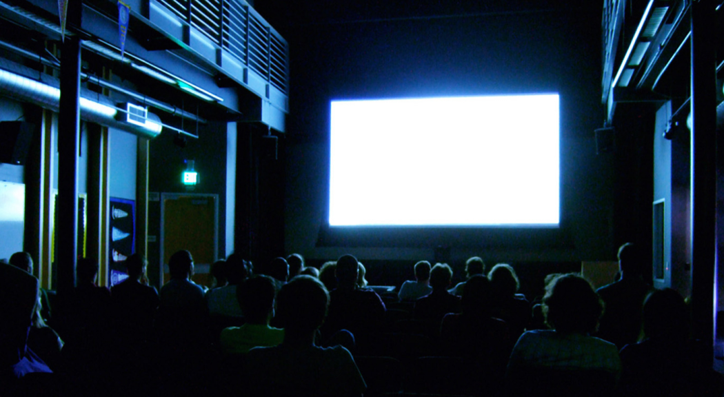 Audiencia en una sala de cine mira una pantalla en blanco.