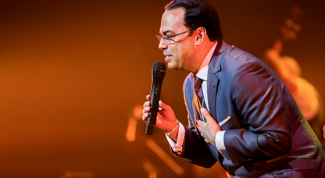 Foto de Gilberto Santa Rosa, vestido de traje entero, en medio de una presentación.