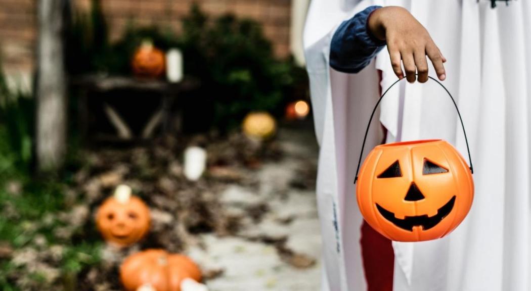 Un niño disfrazado de fantasma sostiene una calabaza de plástico.