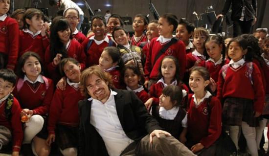 Hombre blanco y rubio posa con estudiantes de colegio.