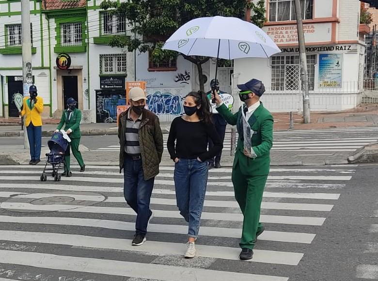 Artistas acompañanado a una peatona mientras hace el cruce en la vía.