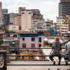 Dos personas jóvenes sentadas en un espacio público, mirando la ciudad. 