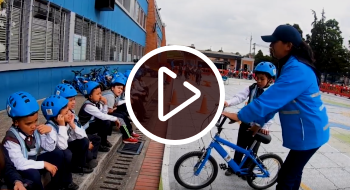 Imagen de una maestra enseñando a los niños a montar bicicleta y respetar normas de tránsito.